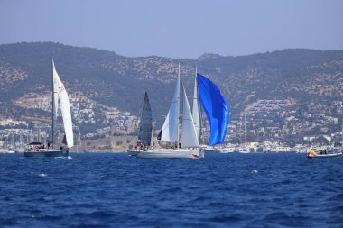 Bodrum, Hindi. 28 Nisan 2024: Yelkenliler Ege Denizi 'nin mavi sularında, ünlü tatil beldesi Bodrum' un kıyılarında rüzgarlı havada yelken açıyorlar..