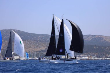 Bodrum, Hindi. 28 Nisan 2024: Yelkenliler Ege Denizi 'nin mavi sularında, ünlü tatil beldesi Bodrum' un kıyılarında rüzgarlı havada yelken açıyorlar..
