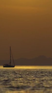 Denizde yelkenli. Denizin üzerinde deniz manzaralı altın gün doğumu. Gündoğumunda yat gezintisi. Güzel bir yelkenli ile deniz manzarası. Yelkenliyle turizm turizmi yapıyor. Dikey video.