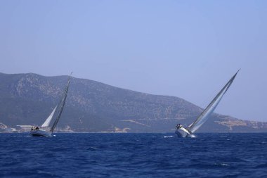 Bodrum, Hindi. 28 Nisan 2024: Yelkenliler Ege Denizi 'nin mavi sularında, ünlü tatil beldesi Bodrum' un kıyılarında rüzgarlı havada yelken açıyorlar..