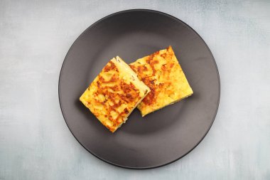 Slices of baked Round Borek cheese pie in kitchen tray with herbs. Dark background. Top view. Copy space