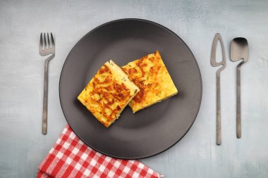 Slices of baked Round Borek cheese pie in kitchen tray with herbs. Dark background. Top view. Copy space