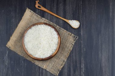 Ahşap arka planda çiğ beyaz pirinç. Ahşap tabakta uzun pişmemiş pirinç. Doğal organik gıda. Geleneksel Asya mısır gevreği kültürü.