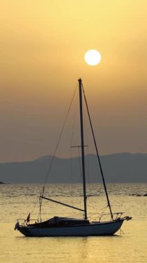 Günbatımında yalnız yelkenli. Turuncu güneşli atmosferik deniz manzarası. Sosyal medya için dikey video. 