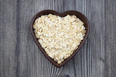 Siyah arka planda kalp şeklinde bir tabakta yulaf ezmesi ve yulaf. Sağlıklı kahvaltı. Organik ve vejetaryen yiyecekler.