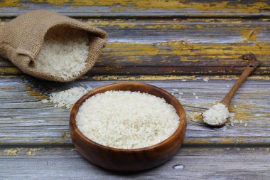 Siyah arka planda çiğ beyaz pirinç. Ahşap tabakta uzun pişmemiş pirinç. Doğal organik gıda. Geleneksel Asya mısır gevreği kültürü.