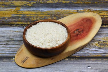 Siyah arka planda çiğ beyaz pirinç. Ahşap tabakta uzun pişmemiş pirinç. Doğal organik gıda. Geleneksel Asya mısır gevreği kültürü.