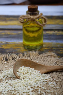 Cam şişe susam yağı ve tahta kaşıkta çiğ susam tohumu ya da kırsal masada kase. Kopya alanı ile pişirilmemiş susam arkaplan kavramı