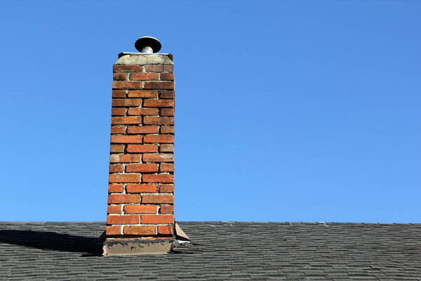 Old Brick chimney against a blue sky on a shingle roof in Canada. 