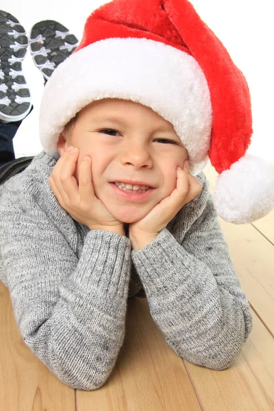 Glücklicher Fünfjähriger Junge Liegt Auf Dem Boden Trägt Eine Weihnachtsmütze Stockfoto