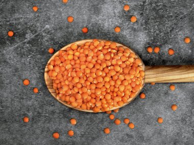 Red lentils in a wooden spoon on grey background, Healthy vegan food concept with high protein. clipart