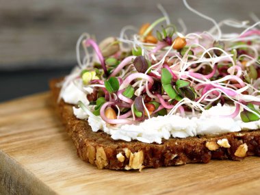 Close up of whole grain bread with cream cheese and sprouts mix on wooden cutting board, healthy breakfast with micro greens.