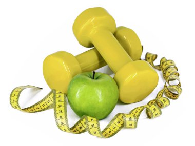 green apple between yellow dumbbells and twisted measuring tape isolated on white background, concept of conscious lifestyle with sport and healthy eating.
