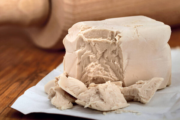 Кубики свежих дрожжей на деревянной доске перед катком, необходимый ингредиент для выпечки хлеба или пиццы.