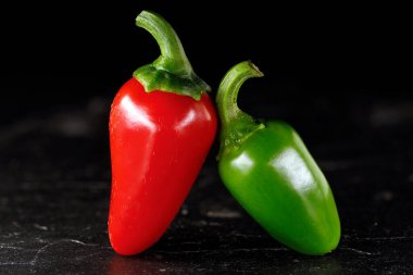 İki acı biber, bir kırmızı ve bir yeşil biber, siyah arka planda yan yana izole..