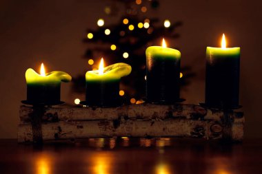 Dört yanan yeşil mum parlayan bir noel ağacının önünde karanlık bir odada sıcak ışıklar altında..