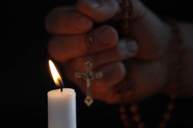 Karanlık arka planda tespih ve dua eden el ile yanan beyaz mum, hasta bir insan ve Tanrı 'ya inanç için dua etmenin dini konsept görüntüsü..