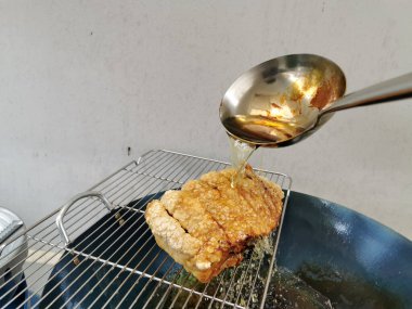 Çıtır domuz eti, mutfakta çıtır çıtır olması için derinin üzerine metal bir kepçeyle kaynar yağ dökülerek pişiriliyor.