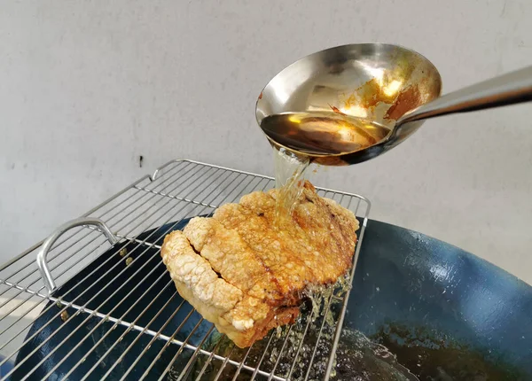 stock image Crispy pork that is being cooked by pouring boiling oil from a metal ladle over the skin to make it crispy in kitchen