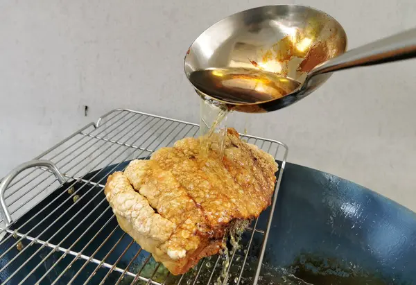 stock image Crispy pork that is being cooked by pouring boiling oil from a metal ladle over the skin to make it crispy in kitchen