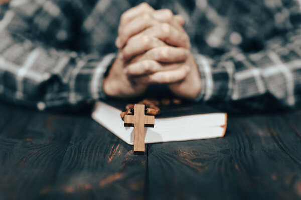 Человек молится на книге с крестом на руках