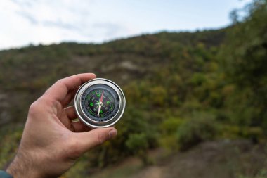 Ormanların ve dağların arka planına karşı bir pusula tutuyor