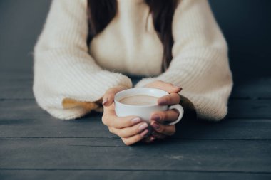Young woman holding a cup of coffee in her hand at the tabl