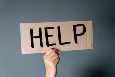 Üzerinde yazı olan bir karton parçası tutan eller. Gri bir sırt grubunda yardım.