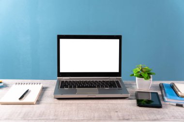 Masanın üzerinde bir dizüstü bilgisayar, bir bitki, bir not defteri ve bir masa.