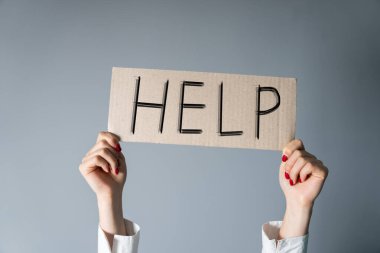 Üzerinde yazı olan bir karton parçası tutan eller. Gri bir sırt grubunda yardım.