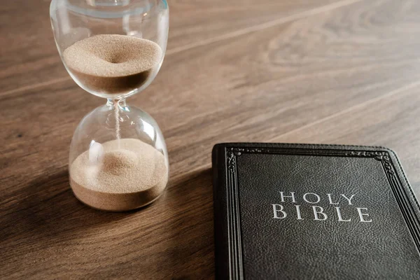 Masanın üzerinde kum saati ve İncil var.