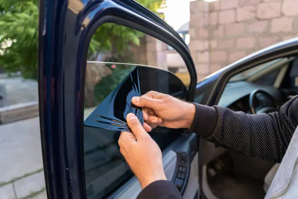 Bir adam arabanın yan camındaki boyayı söker.