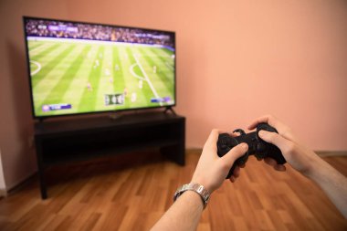 Bir adam evde monitörün önünde otururken joystick ile oynuyor.