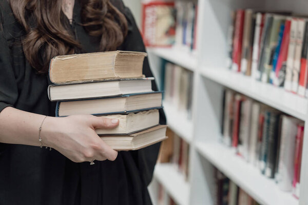 Девушка стоит с кучей книг в руке в либраре