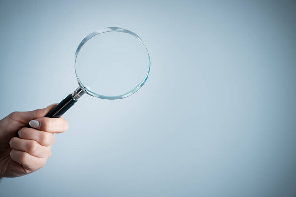 Holding a magnifying glass on a gray backgroun