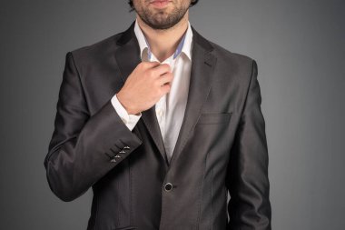 Takım elbiseli bir adam yakasını kanepede düzeltir.