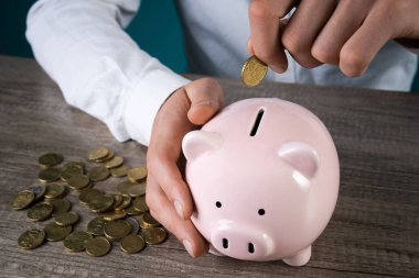 Adamın biri masadaki domuz kumbarasına bozuk para atıyor.