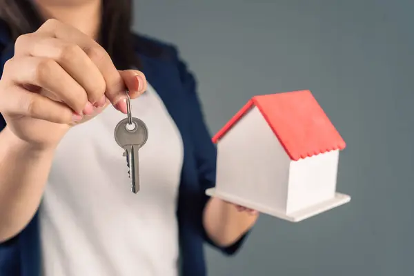 Woman holding house model and keys in hand on gray backgroun