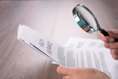 Bir adam masadaki kağıtları büyüteçle inceliyor.