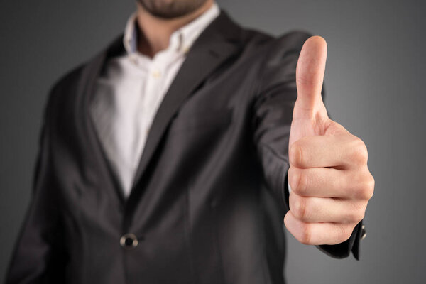 Man in suit showing thumbs up on gray backgroun
