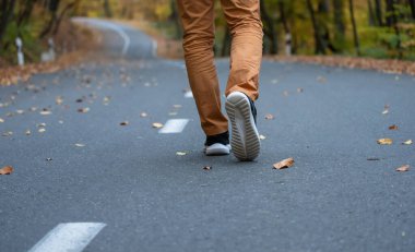 Bir adam asfalt yolda sonbaharda yürür.