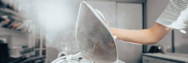 Masadaki elbiseleri ütüleyen kadının elini kapat.