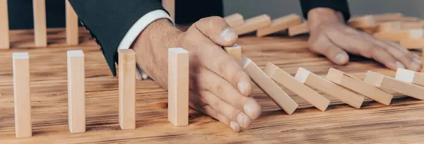 Risk and Strategy in Business, Image of hand stopping falling collapse wooden block dominoes effect from continuous toppled bloc