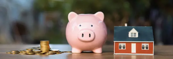 Coins, a piggy bank and a house on a wooden tabl