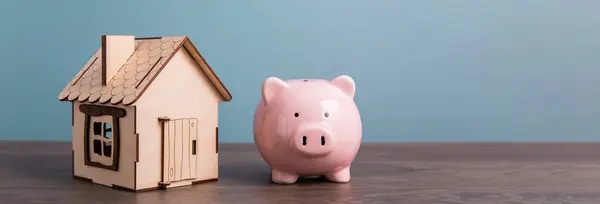 Home model and piggy bank on a wooden table.Saving money exchang