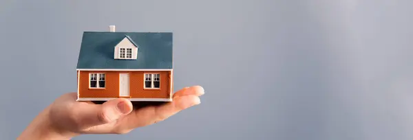 Hand holding house model on grey backgroun