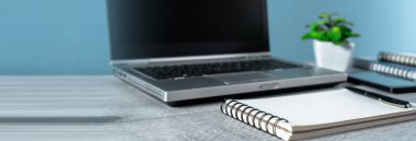 Masanın üzerinde bir dizüstü bilgisayar, bir bitki, bir not defteri ve bir masa.