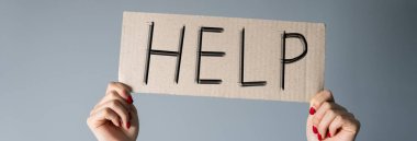 Üzerinde yazı olan bir karton parçası tutan eller. Gri bir sırt grubunda yardım.