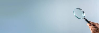 Gri sırtüstü büyüteç tutan genç kadın.