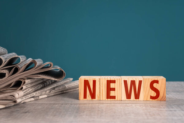 Newspapers and wooden cubes with the word "news" on a blue background stock photo